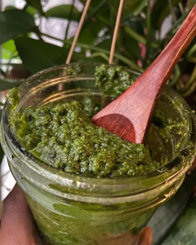 A glass jar of bright green Garden Glow Pesto with a wooden spoon