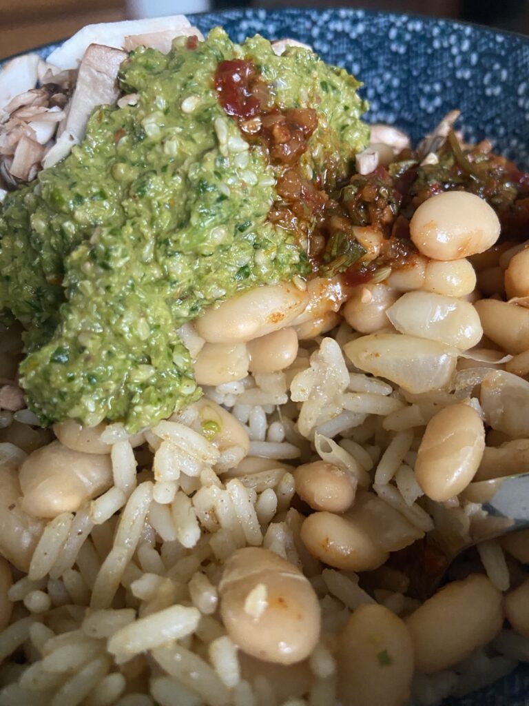 A bowl of rice, white beans and mushrooms topped with a spoonful of bright homemade green herb blend and chili crisp