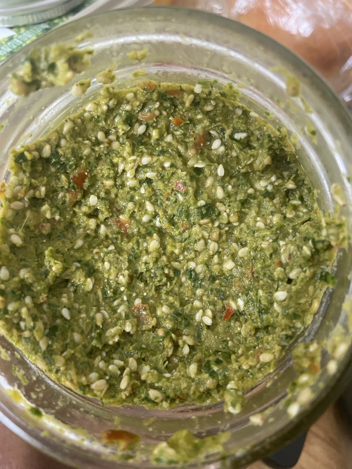 A jar of thick green herb spread studded with sesame seeds and bits of tomato and pepper