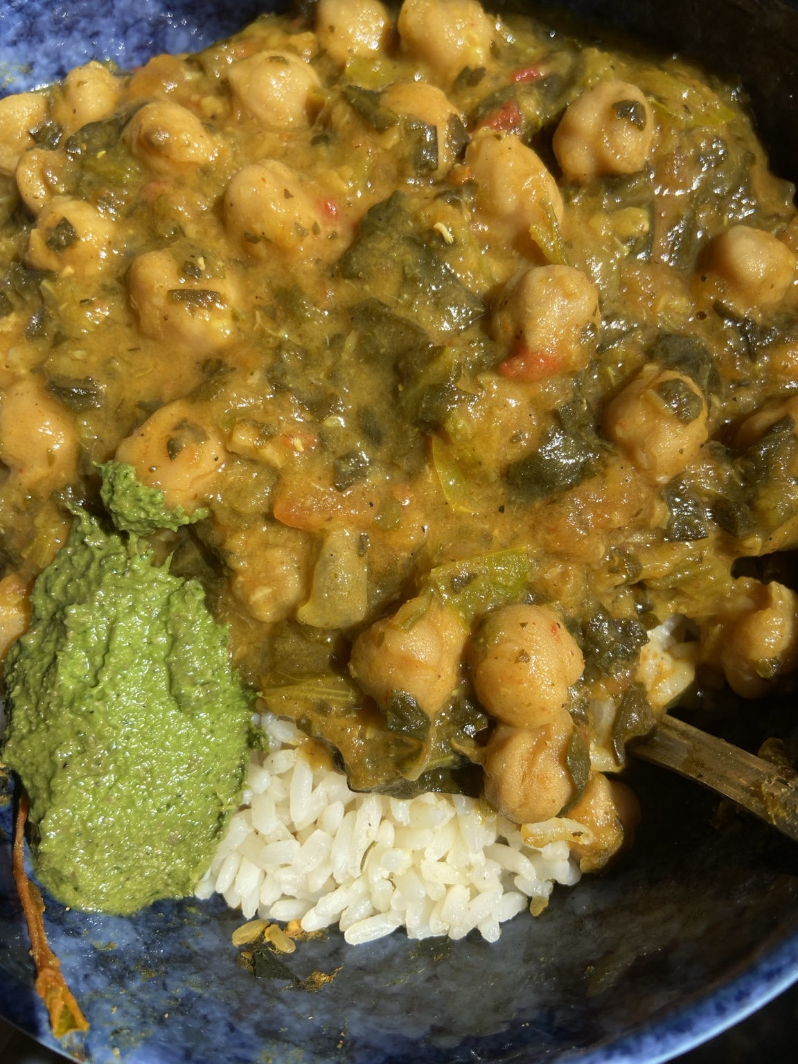 Harissa coconut chickpea stew served over white rice with a spoonful of green herb sauce in a blue bowl
