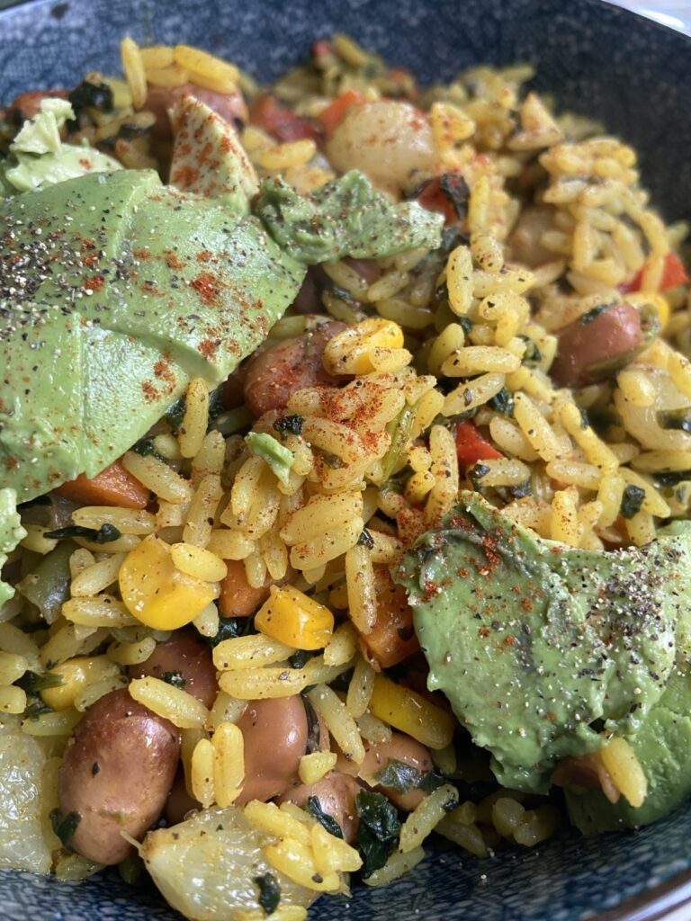 A bowl of turmeric rice with fava beans, vegetables and sliced avocado